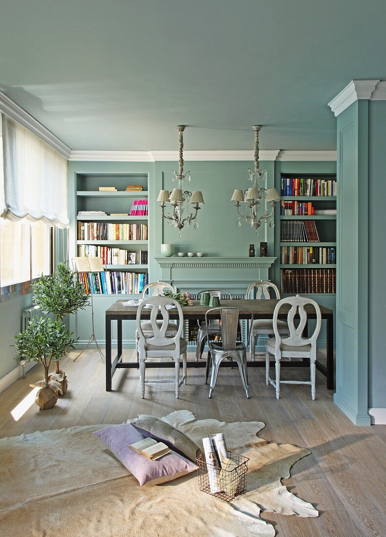 Gemütlicher Platz auf Tierfell am Boden vor Esstisch mit verschiedenen Stühlen in hellblau getöntem Wohnraum mit traditionellem Flair