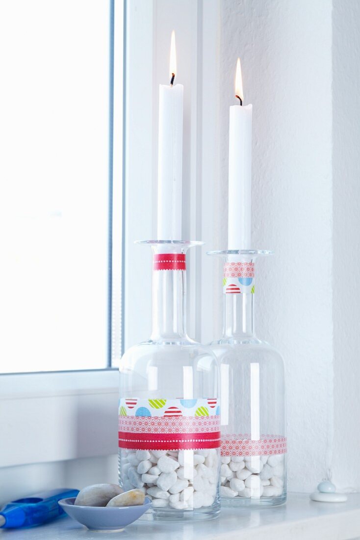 Lit candles in glass bottles with decorative pebbles and stripes of colourful tape as bathroom decoration