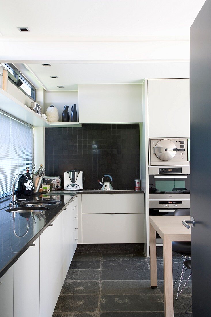 View into modern kitchen with white fitted cupboards and black slate floor