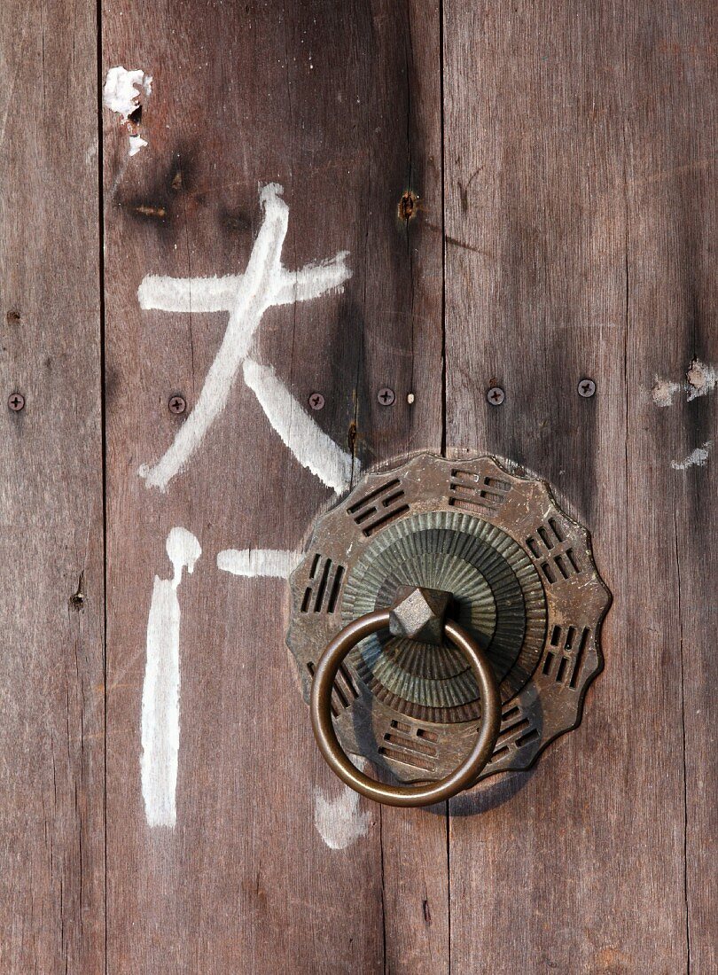 Asiatische Schriftzeichen neben Türklopfer aus Metall an Holztür