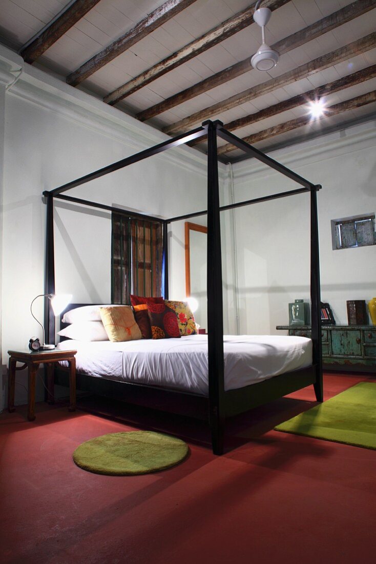 Himmelbett mit schwarzem Holzgestell auf rotem Boden in minimalistischem Schlafzimmer mit Holzbalkendecke