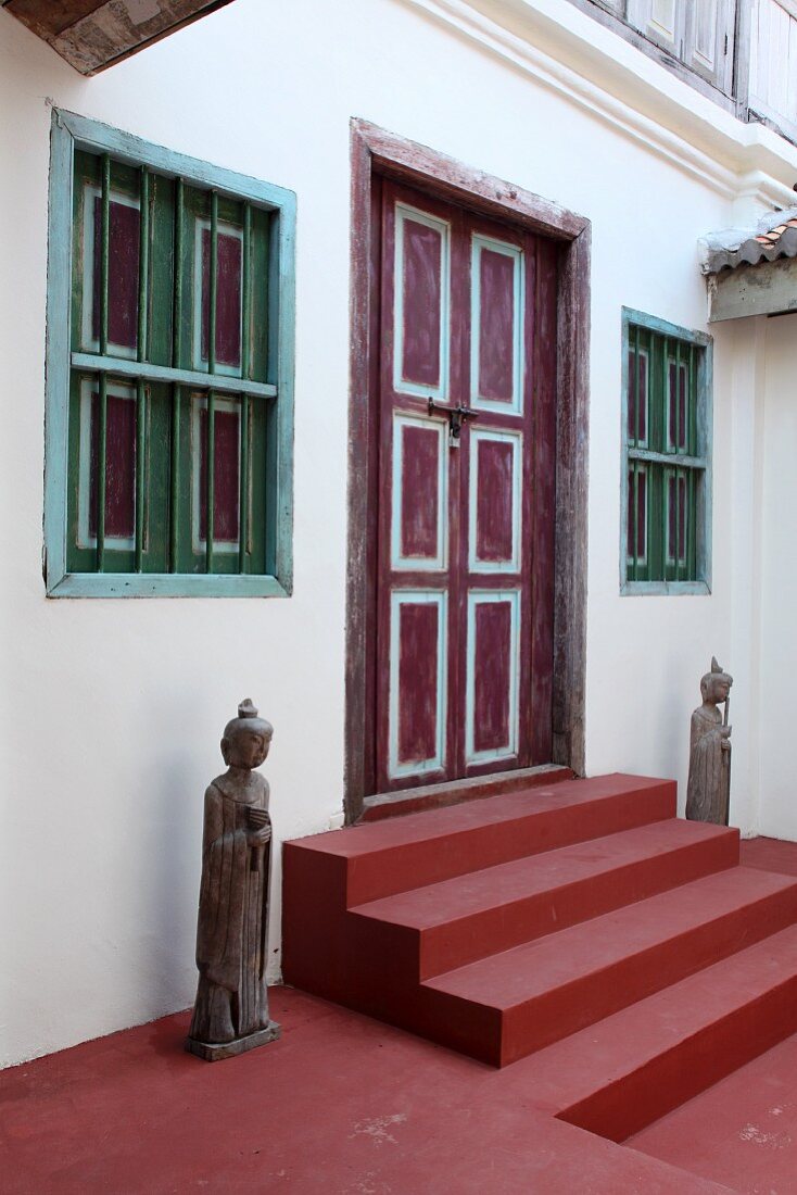 Traditionelle Statuen neben rotgestrichenen Stufen vor bemalter Haustür eines Wohnhauses