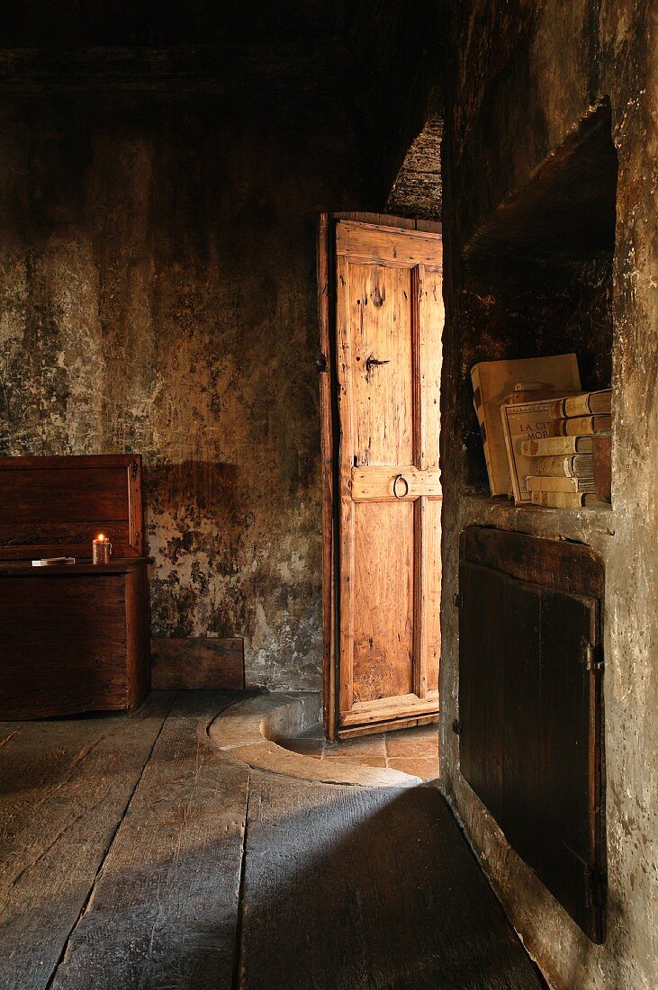 Lichteinfall durch halboffene Holztür in Zimmer eines alten Hauses mit verrussten Wänden