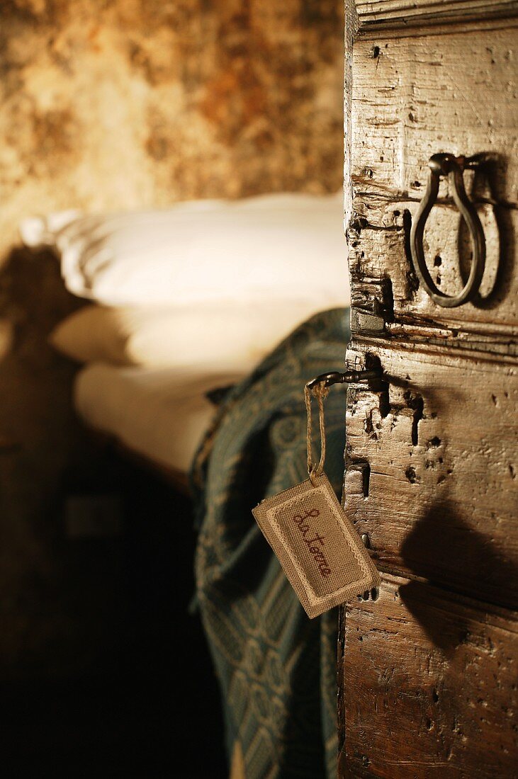 Blick auf Bett durch offene, rustikale Holztür mit Vintage Türgriff und Schild am Schlüssel