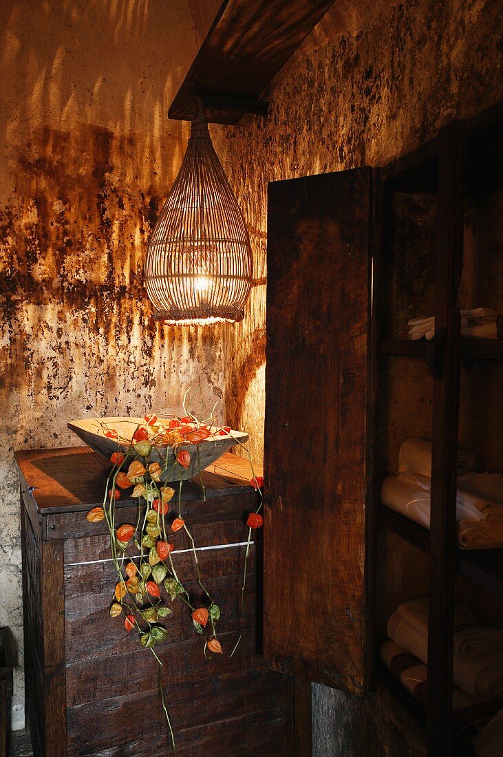 Bowl of physalis on old cabinet and pendant lamp with wicker shade in corner of room