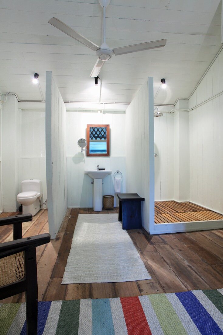 Schlichtes Badezimmer mit Trennwänden zwischen Sanitärbereichen und Deckenpropeller