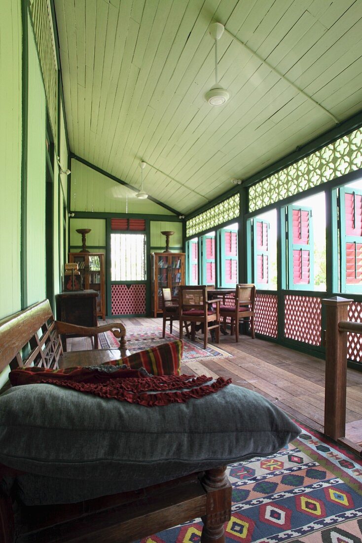 Veranda eines traditionellen asiatischen Holzhauses mit Lochholz Geländer und Sitzbank aus dunklem Holz mit Kissen