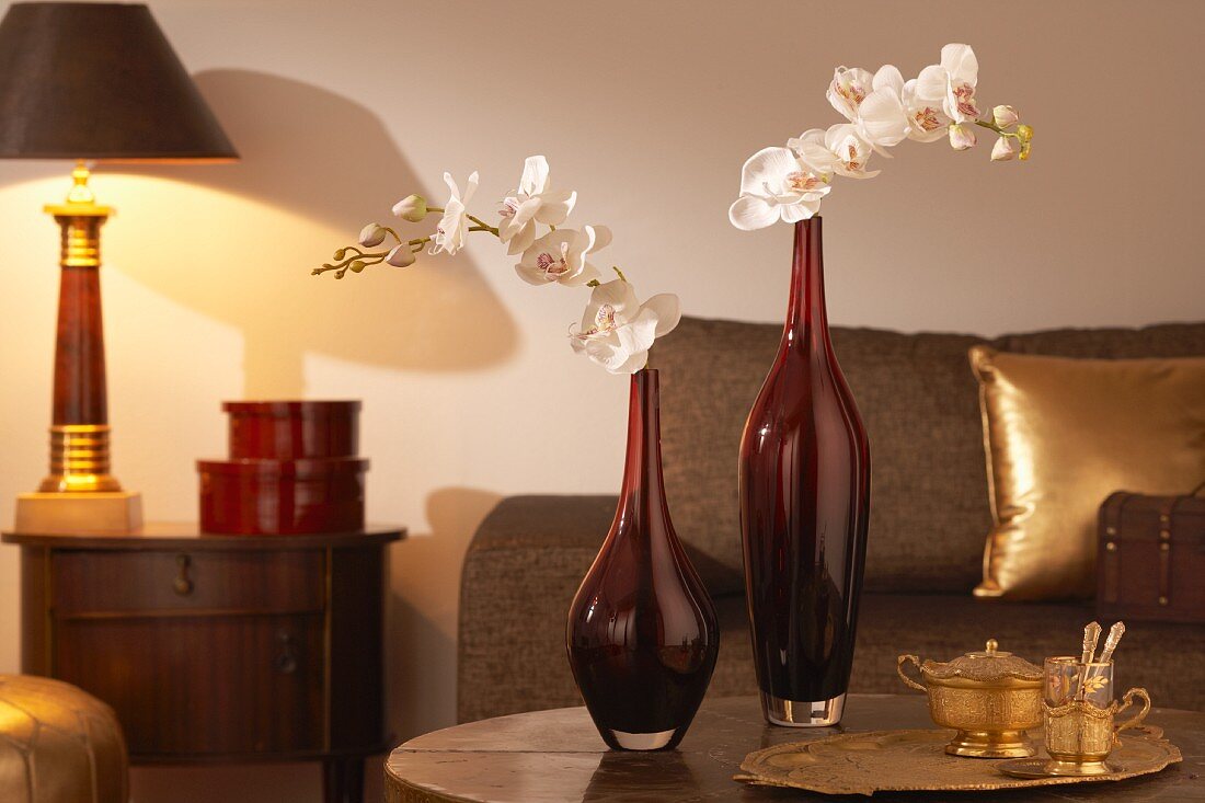 Rote Glasvasen mit Orchideen, Teeglas und Zuckerdose auf Sofatisch