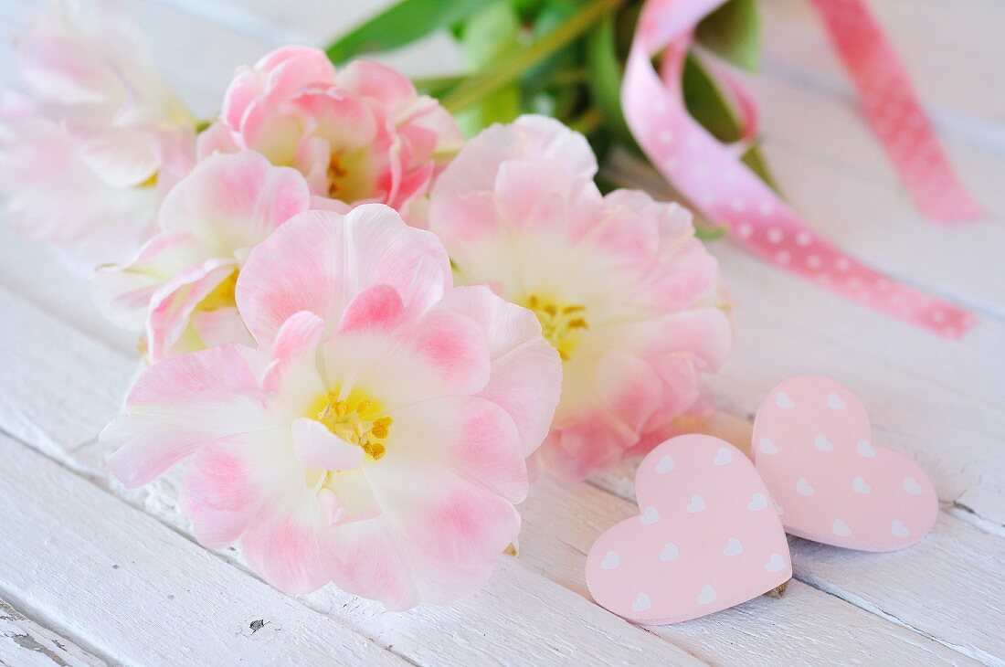 Pink flowers and decorative hearts on white wooden surface