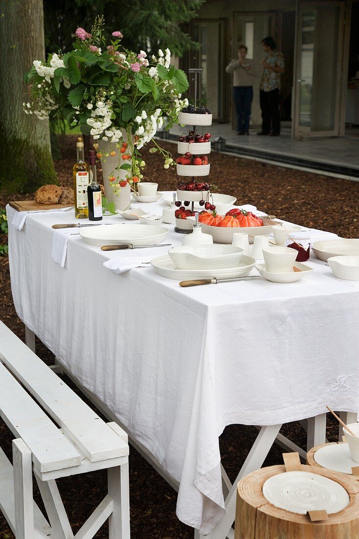 A summery garden table laid with a white cloth with a pebbled yard