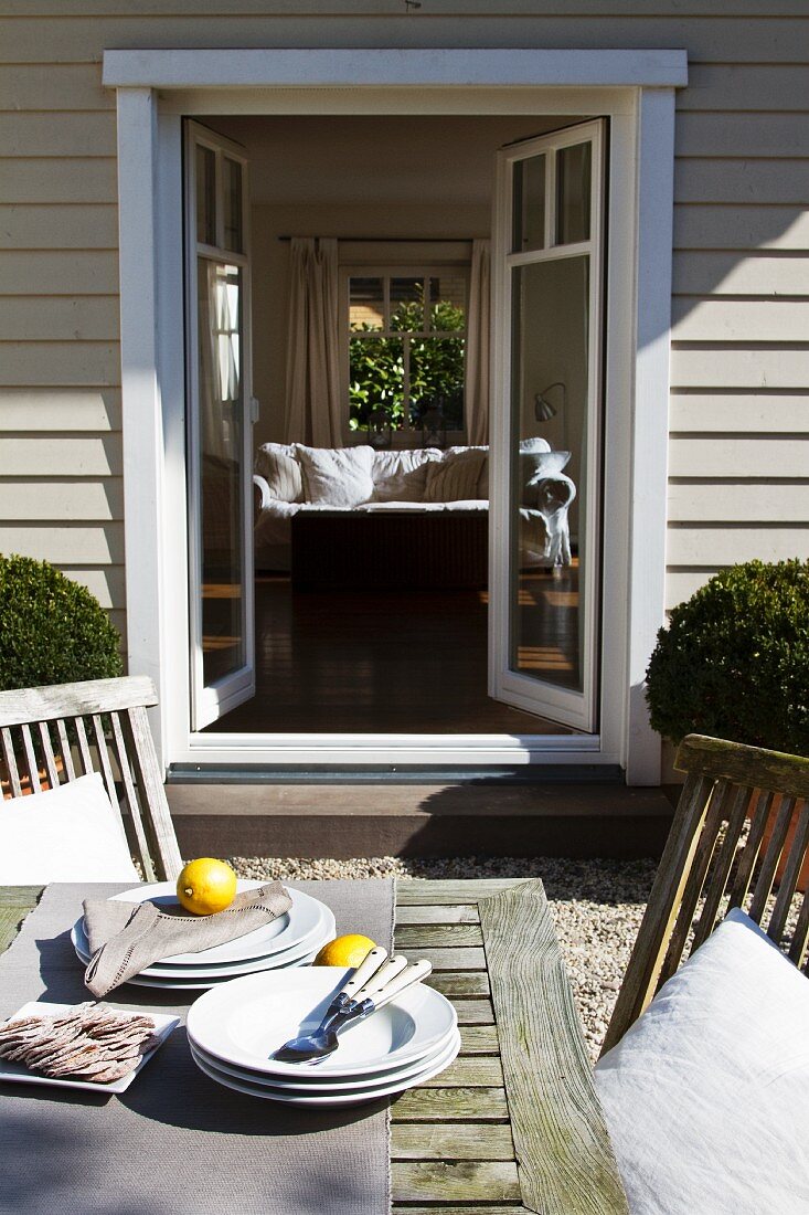 Tisch im Freien mit Tellern und Zitronen vor offener Terrassentür eines Holzhauses und mit Blick in den Wohnraum