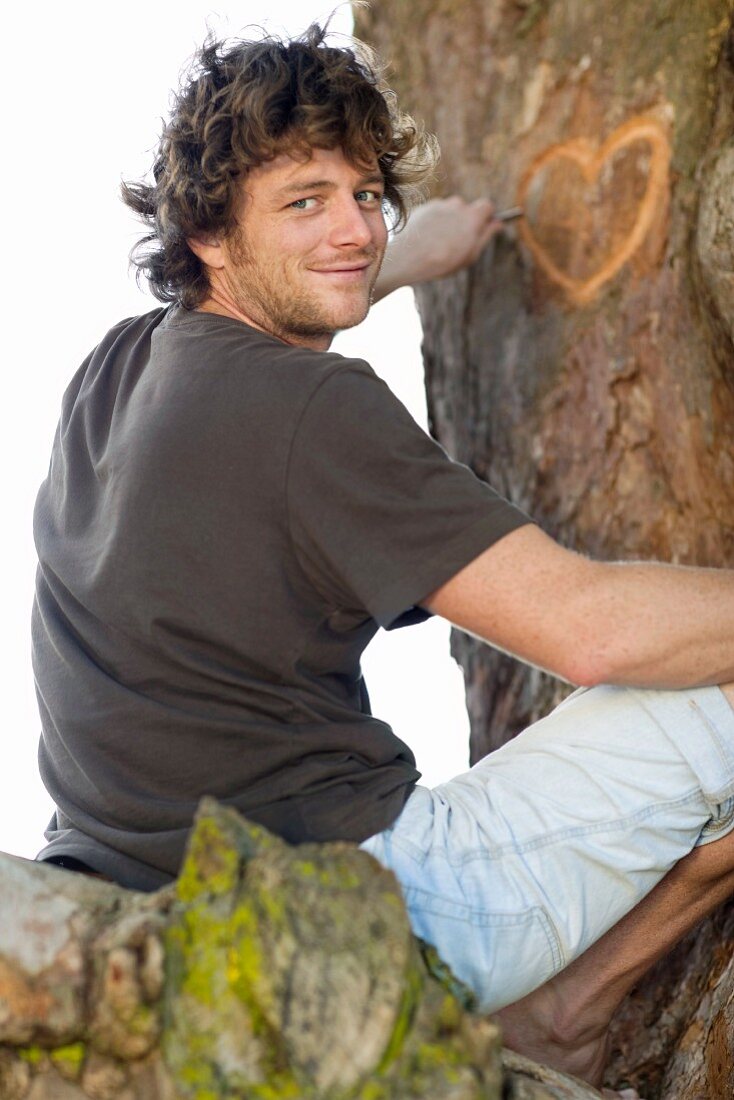 Lächelnder Mann ritzt ein Herz in einen Baumstamm
