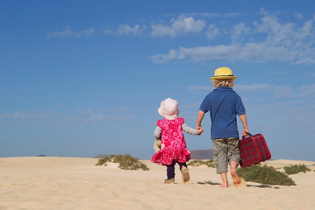 Zwei Kinder gehen mit Koffer am Sandstrand