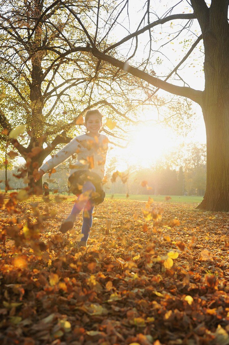 Mädchen spielt mit herbstlichen Blättern im Park
