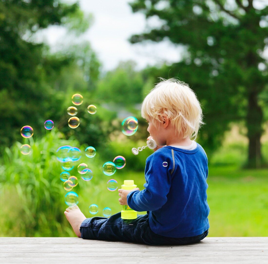 Little boy blowing soap bubbles in garden