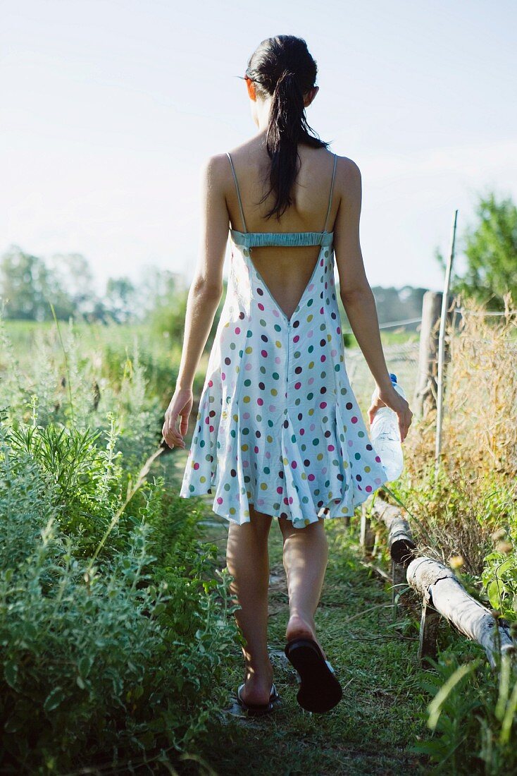 Junge Frau spaziert auf einem Weg zwischen Feldern
