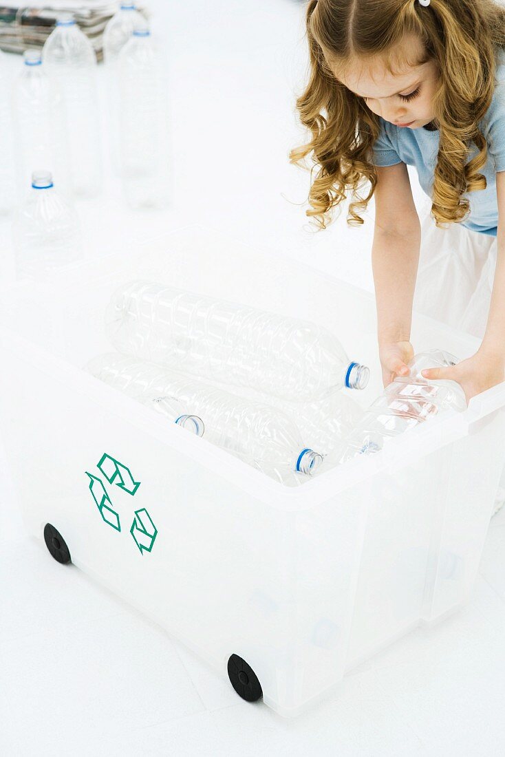 Little girl bending over, placing plastic bottles in recycling bin