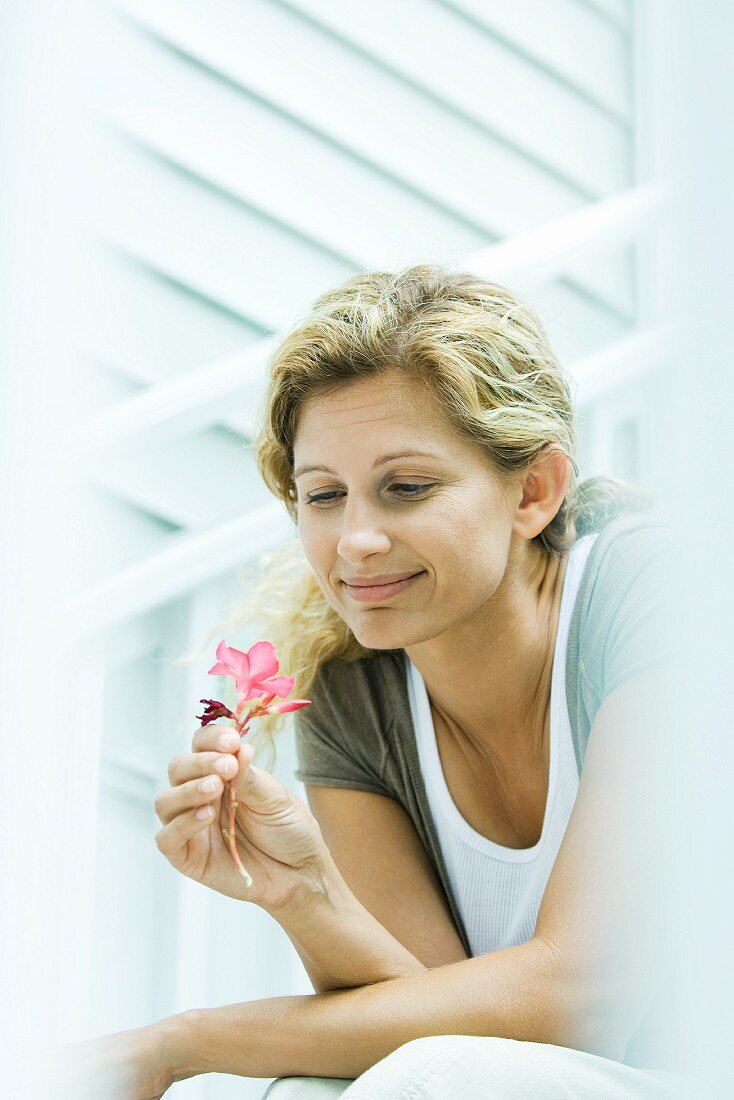 Woman looking down at flower in hand, smiling