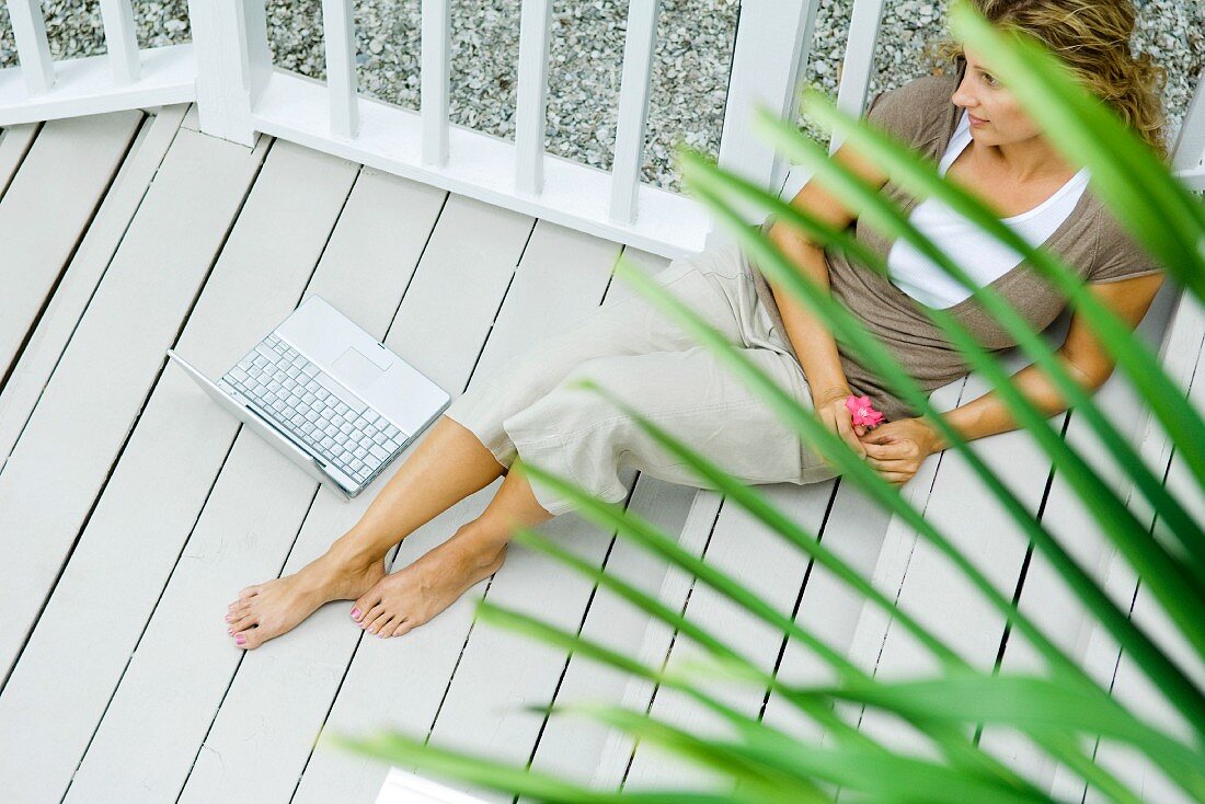 Frau mit Notebook sitzt auf dem Verandaboden