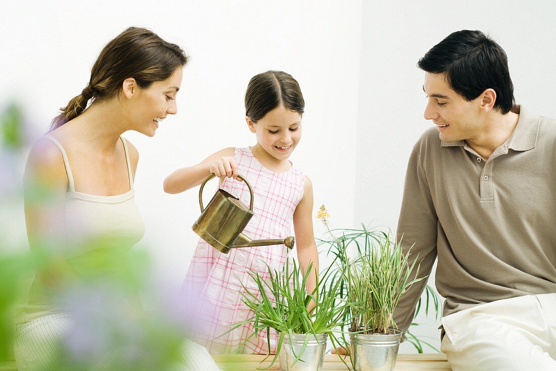 Little girl watering potted plants, parents watching, all smiling