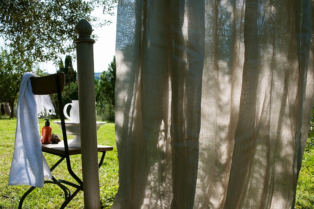 Geschlossener Vorhang teilweise Blick versperrend vor Garten und Stuhl mit Waschaccessoires