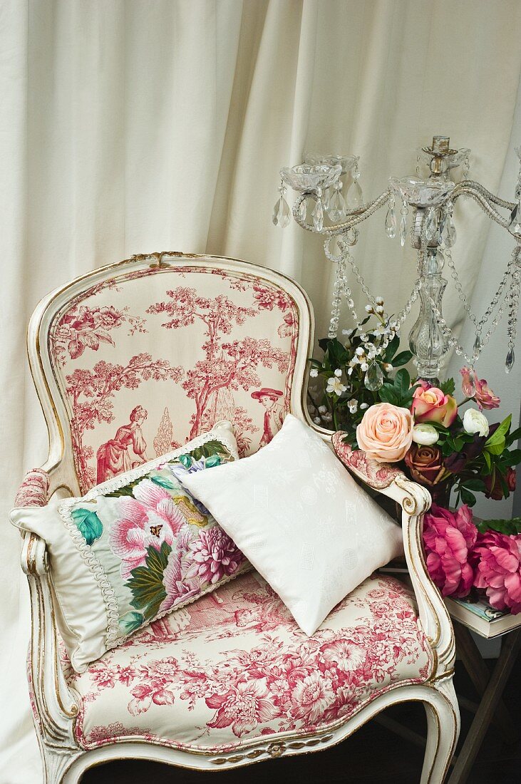 Rococo-style armchair next to flowers and candelabra with glass ornaments