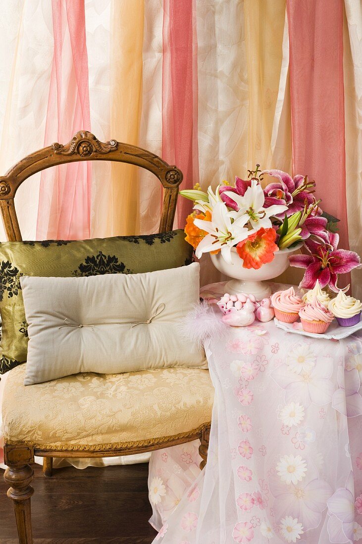 Cushions on antique chair next to side table with floor-length tablecloth and bouquet