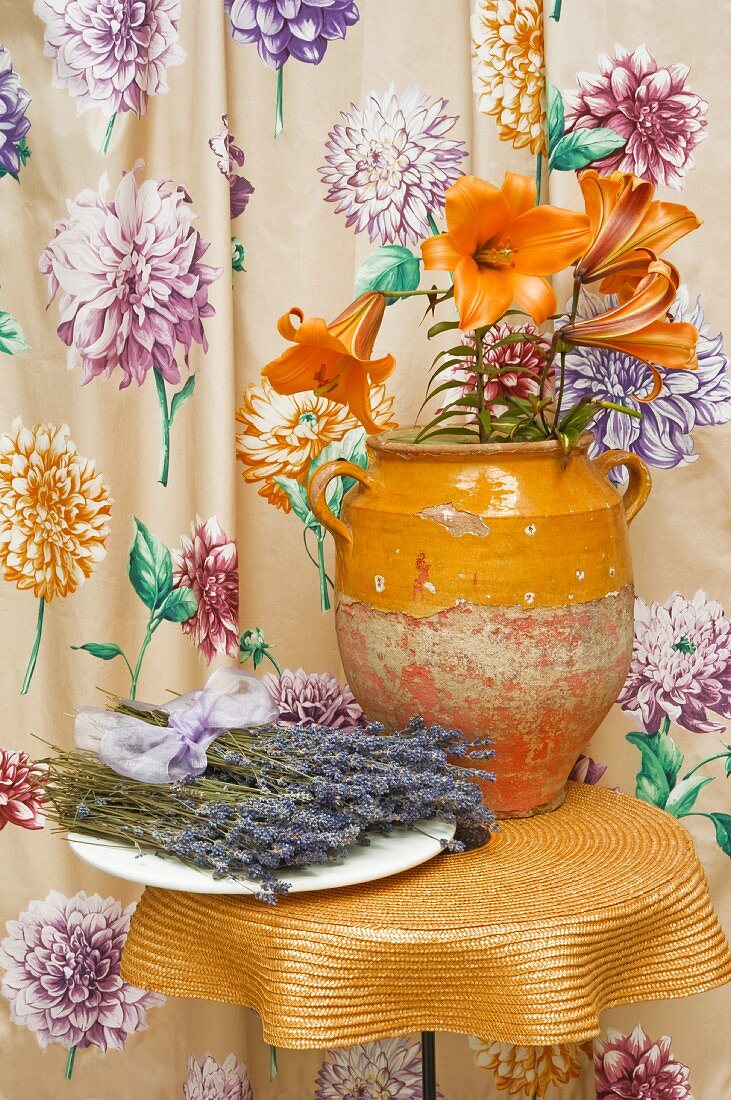 Rustikale Tonvase mit Blumen auf Beistelltisch vor geblümten Vorhang