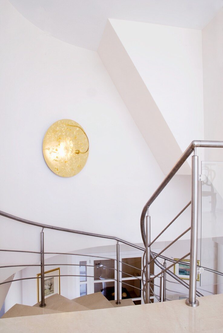 Goldene Wandleuchte an Treppenhauswand und Blick von oben auf Treppe mit Edelstahlgeländer