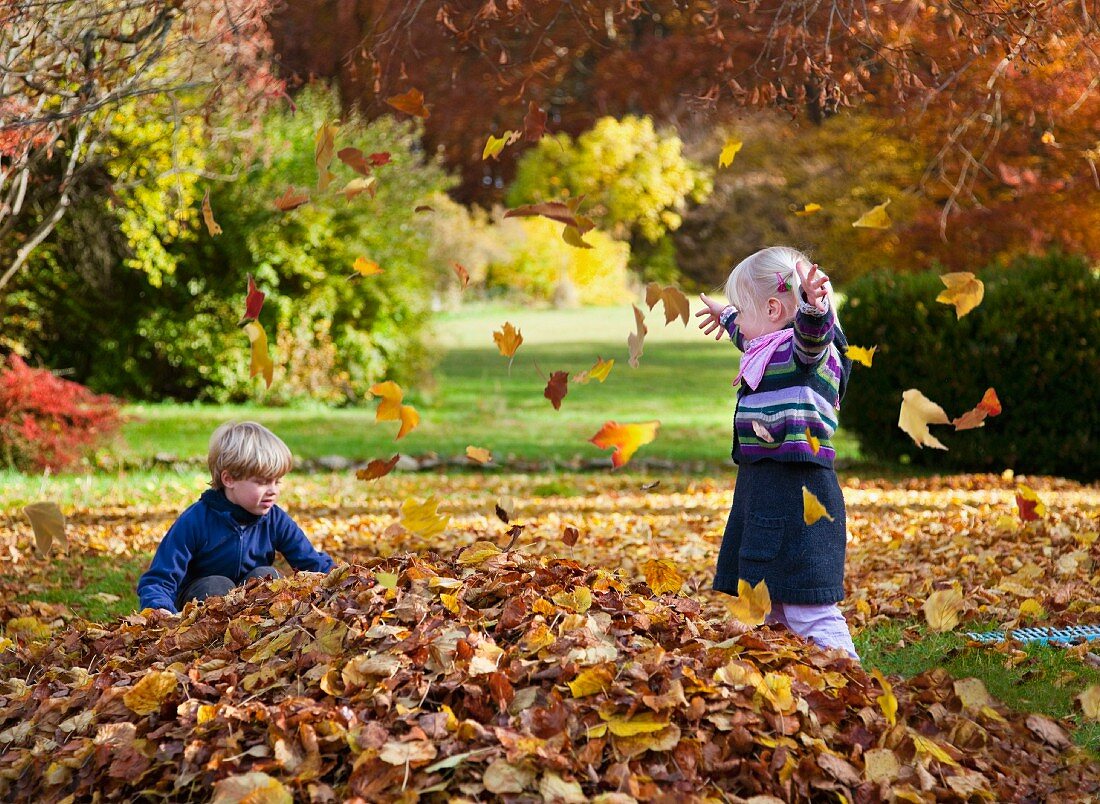 Kinder spielen mit herbstlichen Blättern im Park