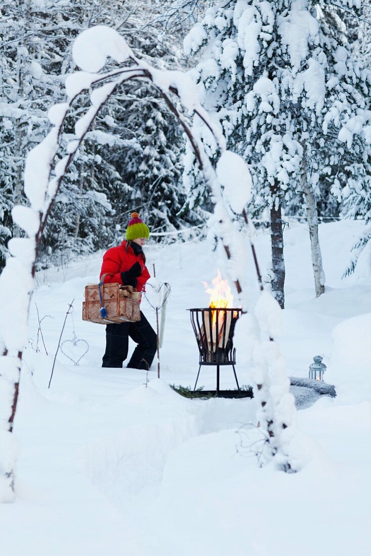 Frau trägt Picknickkorb zum Feuerkorb im verschneiten Garten