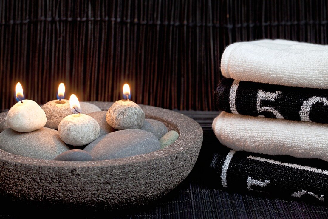 Relaxation in spa - lit pebble candles in stone dish next to stacked towels