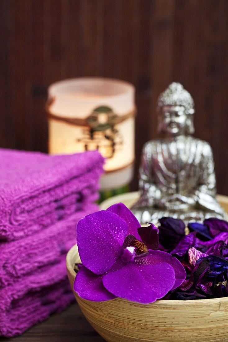 Meditative Stimmung im Spa - violette Orchideenblüten in Bambusschale und Buddhafigur im Hintergrund