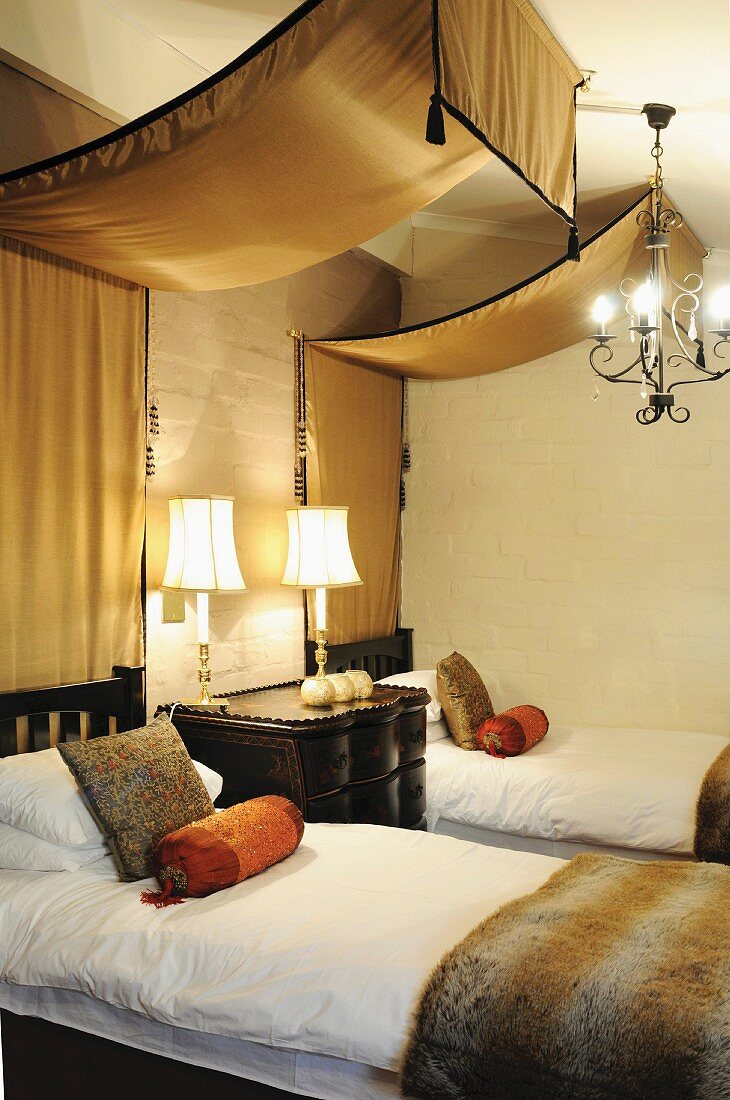 Bedroom in warm earthy shades - golden brown silk canopies above twin beds made of dark, African wood