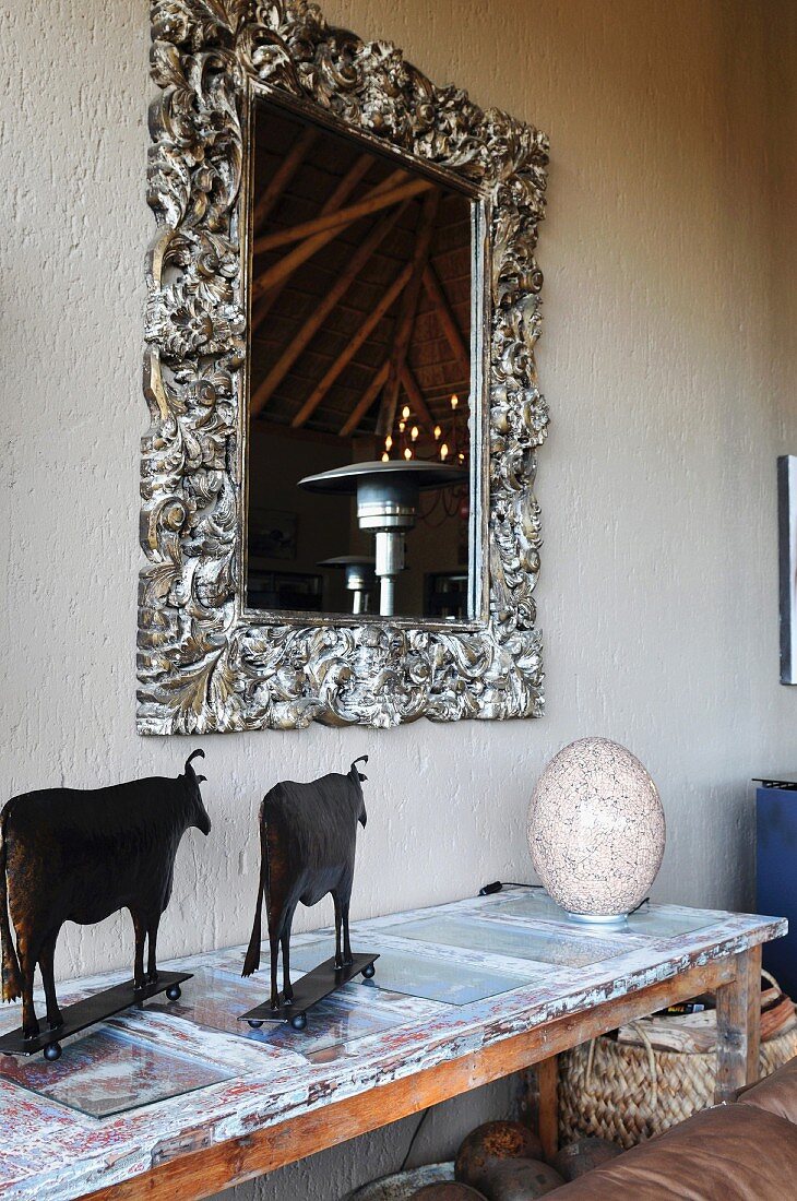 Mirror with silver, ornamental frame above African cattle ornaments on console table