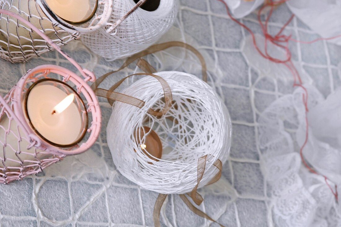 Top view of white lantern made of twine next to two lit candles in wire lanterns