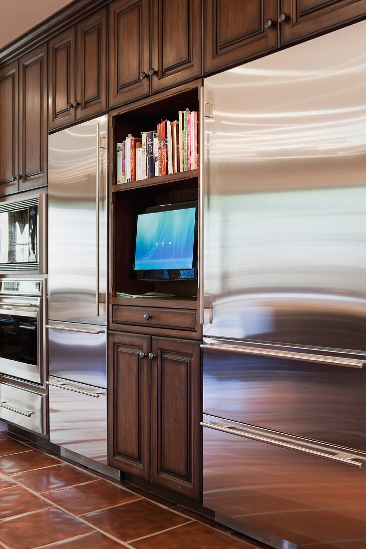 Stilmix in der Küche - Einbauschrank mit Kassettentüren aus dunklem Holz, unterbrochen von modernen Edelstahlfronten