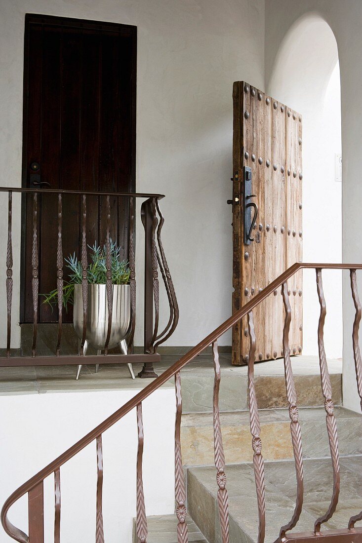 Natursteintreppe mit schmiedeeisernem Geländer und offene, rustikale Eingangstür in mediterranem Wohnhaus