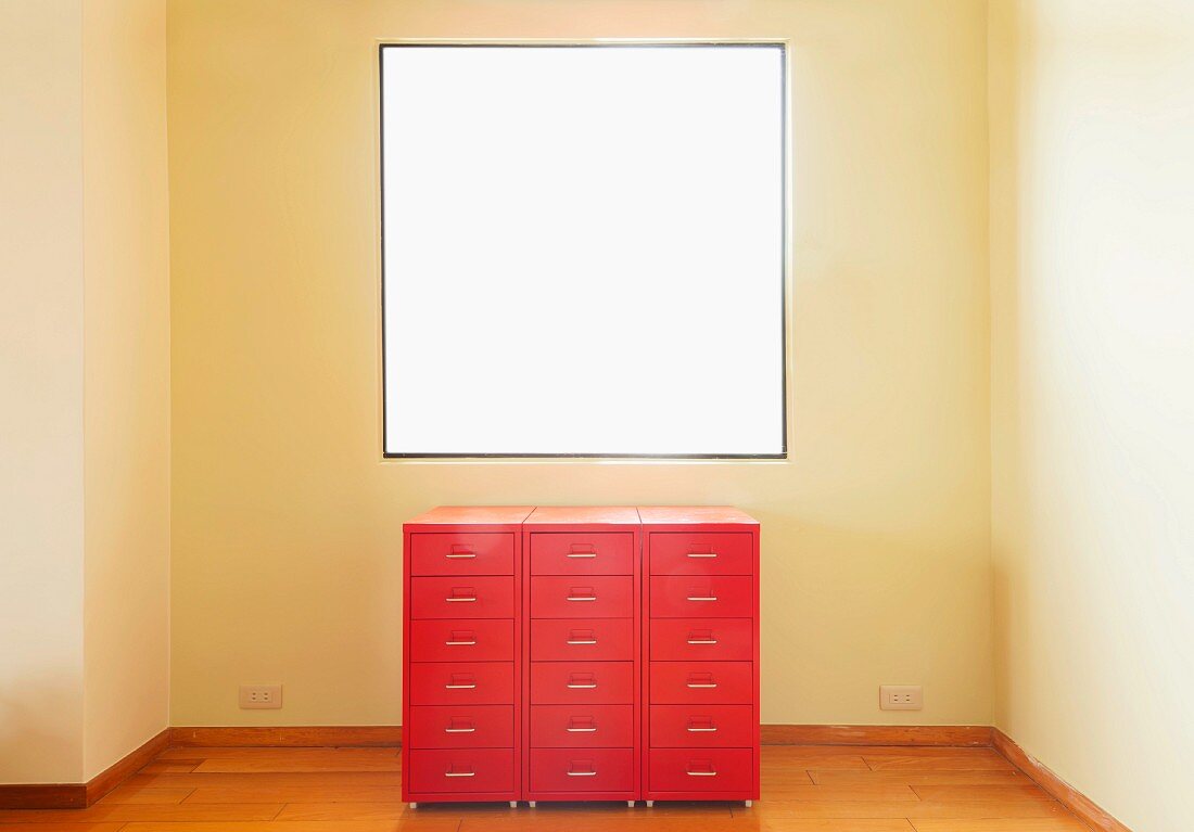 A red chest of drawers in front of a window in an otherwise empty room