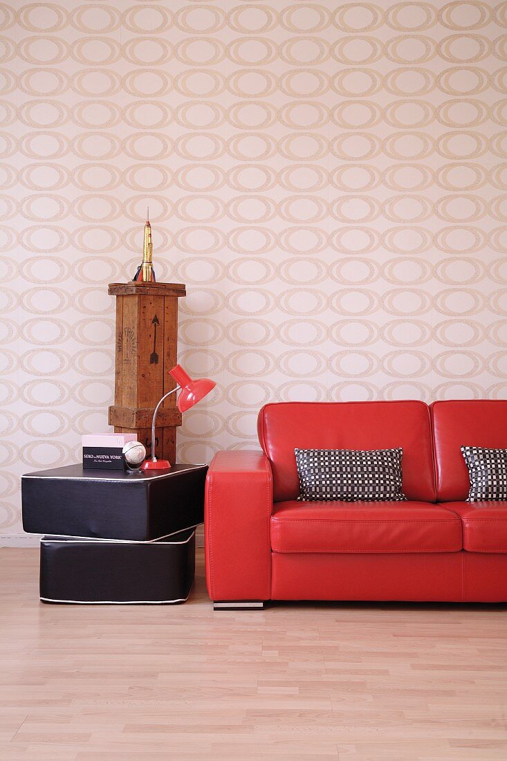 Teilweise sichtbare rote Lack Couch neben gestapelten Bodenpolstern mit Tischlampe vor Wand mit Opart Tapete