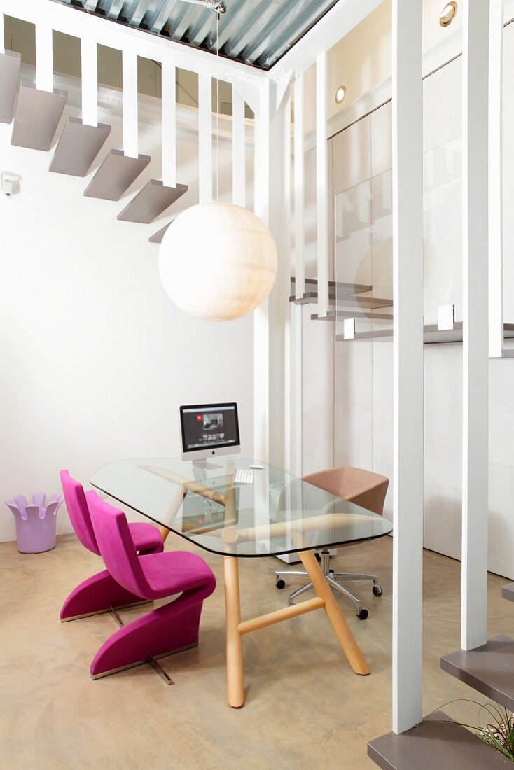Schlichter Glastisch und pinkfarbene Polsterstühle im Arbeitszimmer und Blick auf gewendelten Treppenaufgang
