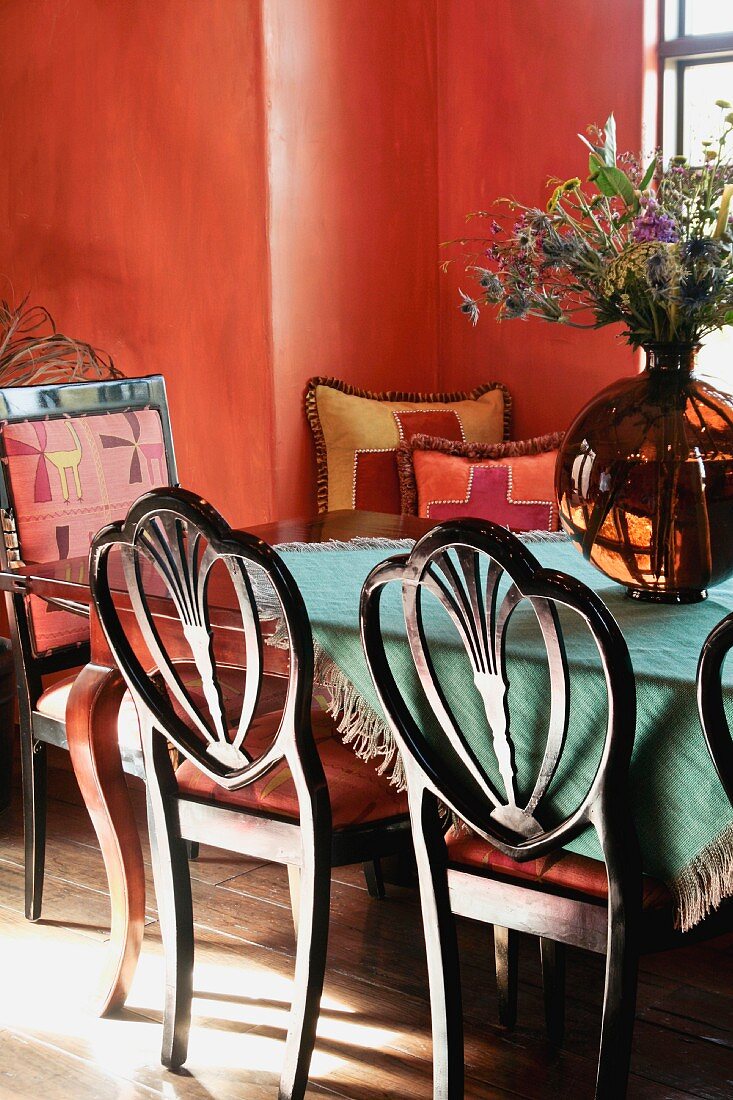 Stühle mit geschwungener Rückenlehne und antiker Tisch in rot getönter Esszimmerecke