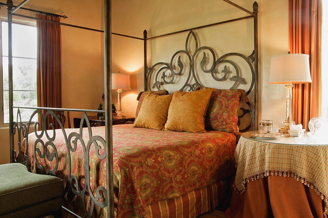 Kissen und elegante Tagesdecke auf Himmelbett mit Metallgestell in schlichtem Schlafraum