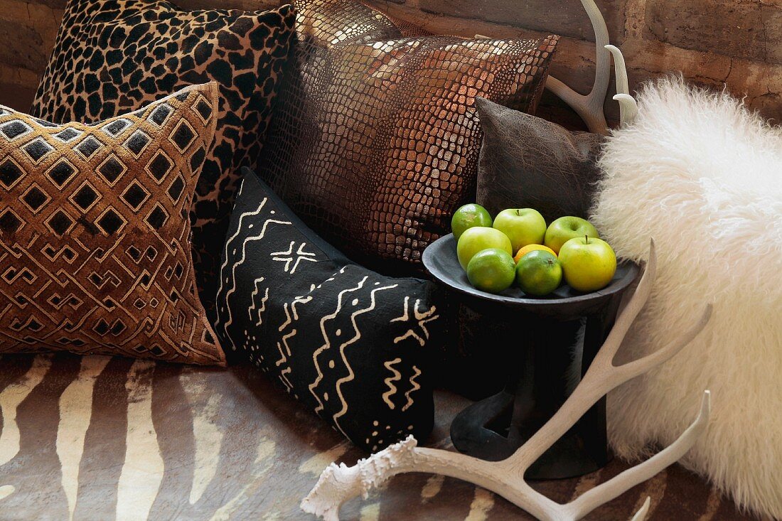 Verschiedene Kissen in afrikanischem Stil und Äpfel auf Beistelltisch aus dunklem Holz