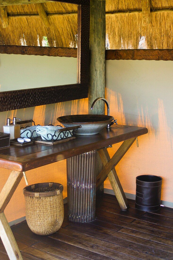 Rustikaler Waschtisch mit Schüssel und Spiegel in afrikanischer Hütte mit Strohdach