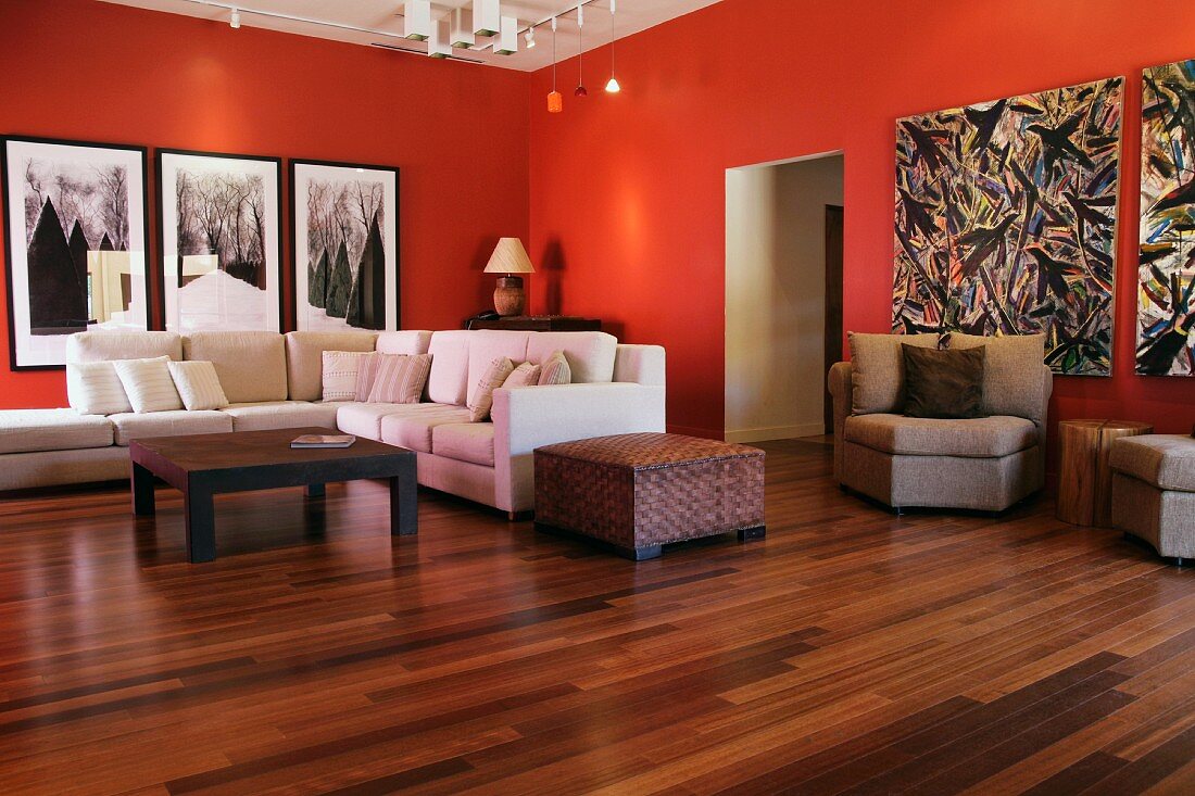 Wohnraum mit modernen Bildern auf rot getönten Wänden und helle Polstergarnitur auf Nussholzparkett