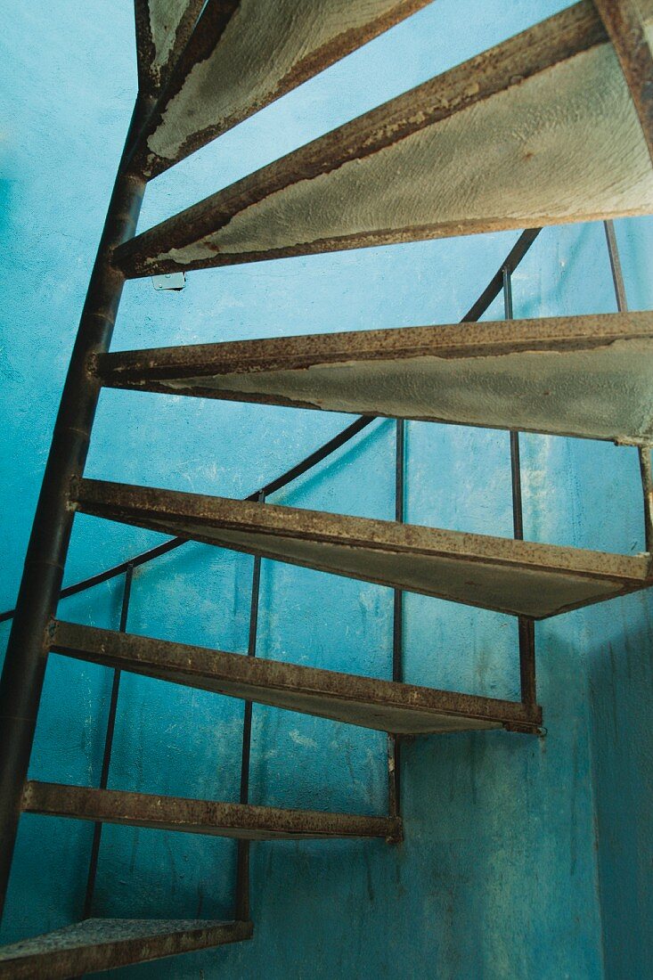 Wendeltreppe mit Spindel aus Metall in Vintagelook vor blau getönter Wand