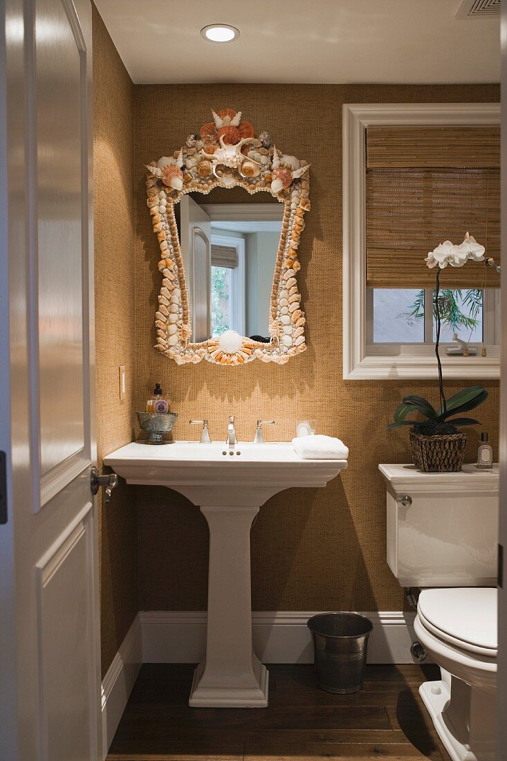 Blick in traditionelles Bad auf Standwaschbecken und Spiegel mit Muscheldekor auf Rahmen