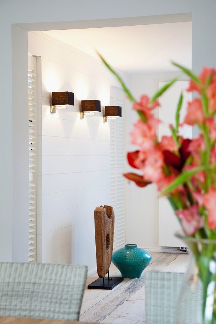 Bouquet of gladioli in dining room and view of modern sconce lamps through wide doorway