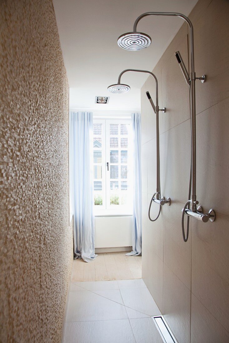 Shower heads in narrow shower area and view of window with floor-length curtains